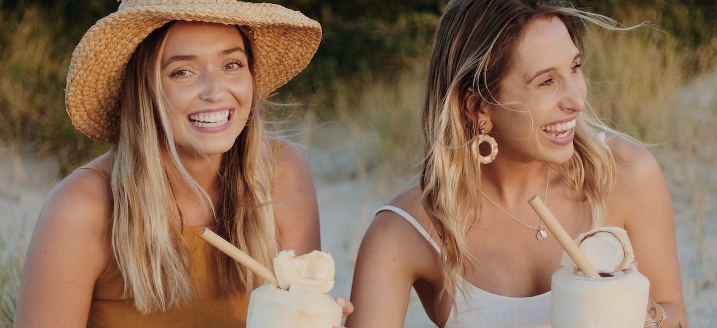 two girls drinking from a coconut with theotherstraw reusable bamboo straws
